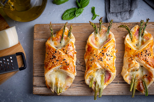 Baked green asparagus with ham and cheese in puff pastry sprinkled with sesame seeds and green basil leaves.