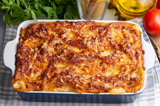 Pasta casserole bechamel sauce topped with melted mozzarella cheese and served in a white baking dish on a table (Turkish name; firinda makarna or firin makarna)