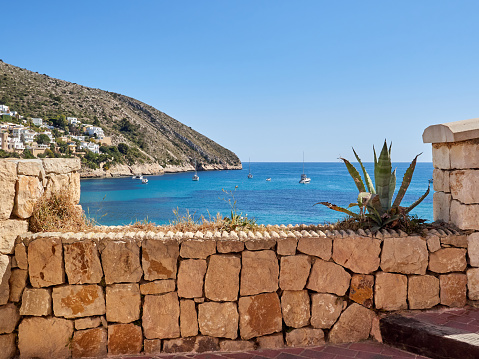 Landscape of the turquoise water of the Mediterranean sea gehind a stone wall in El Portet, a beautiful beach in Teulada Moraira. Costa Blanca, province of Alicante, Comunidad valenciana, Spain, Europe