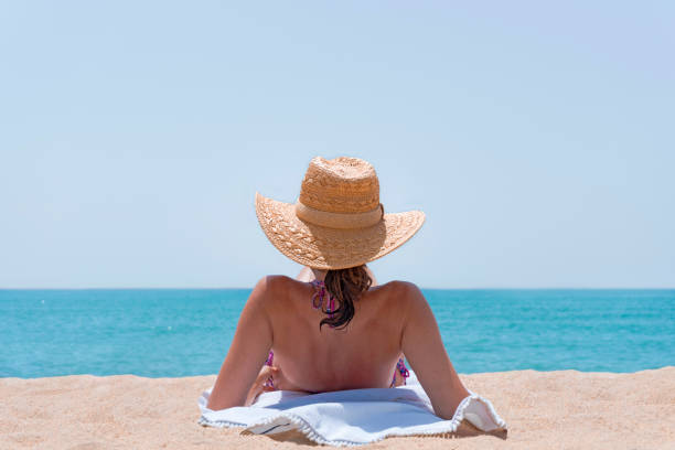 GIRL WITH HAT IN BIKINI SUNBATHING ISOLATED ON THE BEACH.