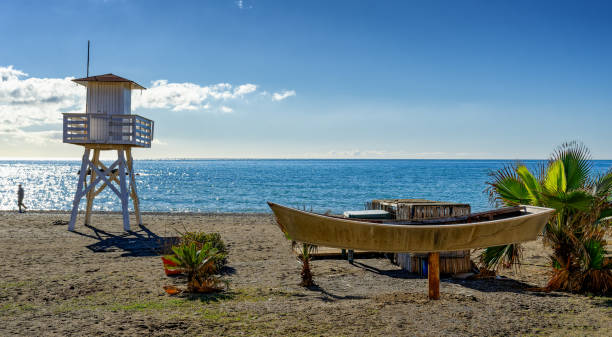 View of the Mediterranean beach of Cala del Moral in Malaga, Spain, with lifeguard tower and boat ashore in a sunny day.