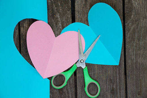 two paper blue and pink hearts and cutted scissors lies on a wooden background close up