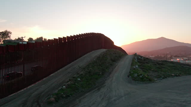 International Border Wall Between Tecate California and Tecate Mexico Near Tijuana Baja California Norte at Dusk Under Stunning Sunset with View of the City From the USA