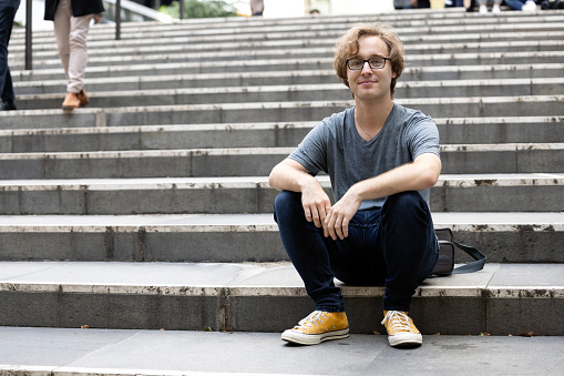 Portrait of  26 years old man with eyeglasses sitting on stairs, background with copy space, full frame horizontal composition