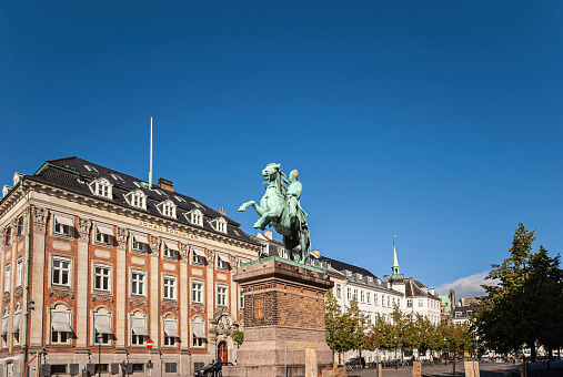 Copenhagen, Denmark - September 15, 2010: Equestrian statue of Absalon on tall pedestal stands on Hojbro Plads in front of Historic mansion of Matrikel1 community club under blue sky.