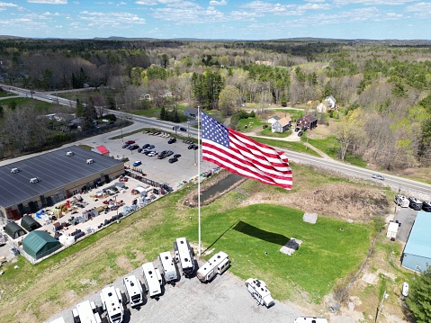 An aerial view of a vibrant landscape of a field in the countryside, with several trucks, cars, and the U.S. flag in the foreground
