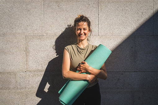 One caucasian woman hold yoga mat while stand outdoor in sunny day