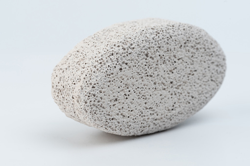 Close-up  of small round object made of cement or stone with Rough and porous surface with pits and bumps on white surface
