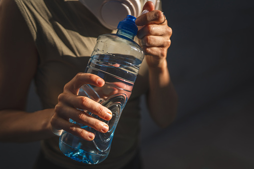 close up on hands midsection of unknown caucasian woman open plastic bottle of water while stand outdoor in sunny day