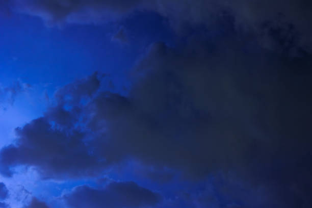 The clouds move fast across the dark night sky, the flashes of light from the approaching storm illuminate them.