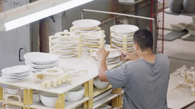 Man staying ceramic plates on a drying shelf in a pottery workshop