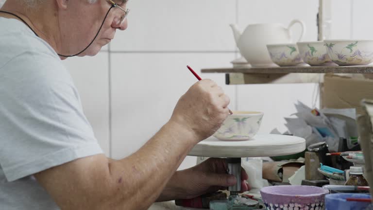 Worker painting a vase at a bench in a ceramics workshop