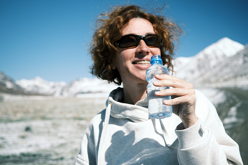 Cheerful female tourist is resting on mountain pass and drinking water