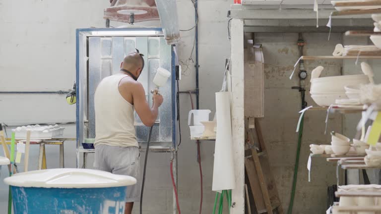 Worker glazing a tray with a spray gun in a ceramics factory