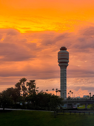During the sunset, a passenger on a commercial airline is treated to a captivating view of the Orlando International Airport's traffic control tower amid vibrant orange sunset clouds.