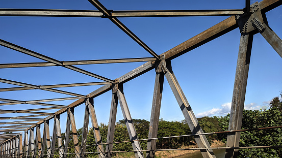 Steel frame construction of a pedestrian bridge in the daytime with small hills and blue sky in the background