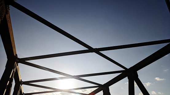 Steel frame construction of a pedestrian bridge at sunset with small hills and evening sky and sun in the background