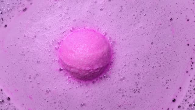 Pink bath bomb ball dissolves in water with foam bubbles.