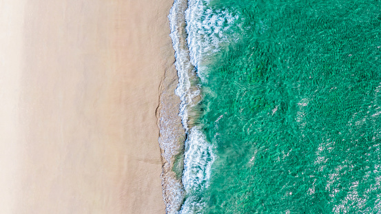 Beautiful quiet white beach background with emerald green waters. Aerial view from above of sea and sand.