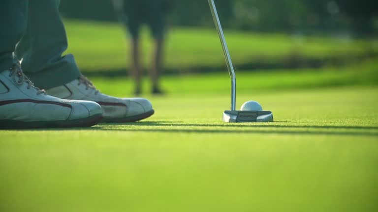 Active professional golfer hits golf ball with club on a putting green golf course.