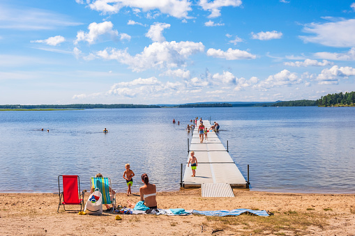 Karlsborg, Sweden-July, 2019: Sunbathing people on a sandy beach by a lake with a jetty and children