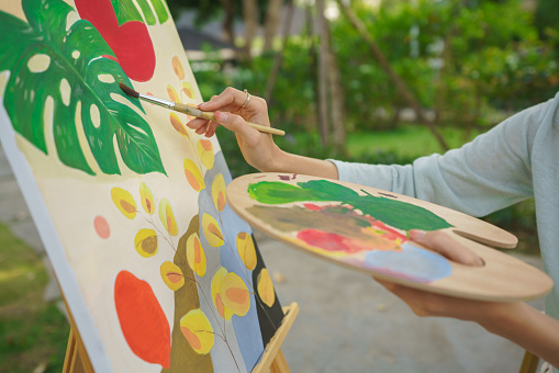 Outdoor activity concept, Female artist holds color palette and brush to painting picture on canvas.