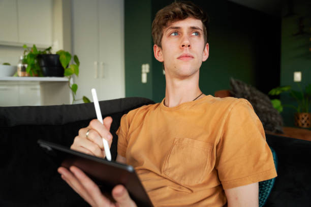istock Young caucasian man in t-shirt looking away while using digitized pen with digital tablet at home 1508582774
