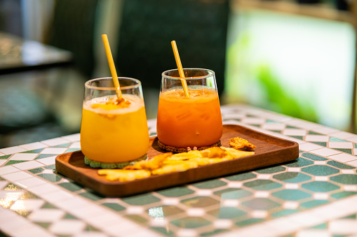 Fresh pineapple and carrot juice in glass cup on a wooden reamer. Selective focus
