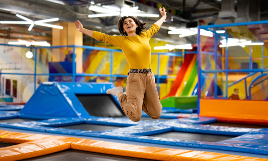 Pretty girl jumping on colorful trampoline at playground park and smiling. Beautiful young woman during active entertaiments