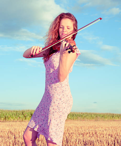 istock Redhead woman playing violin outdoors on the field. Split toning 150865312