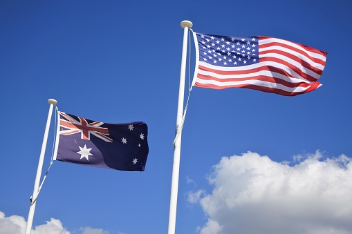 Flag of United States of America fly beside the flag of Australia against clear blue sky. American Foreign relationship policy concept. No people. Copy space