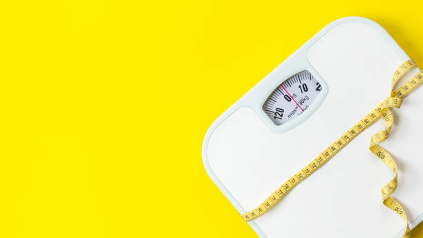 istock Weight loss control planning.  White scale and measuring tape for body dieting healthy life.  Yellow background. Top view copy space for banner 1508676708
