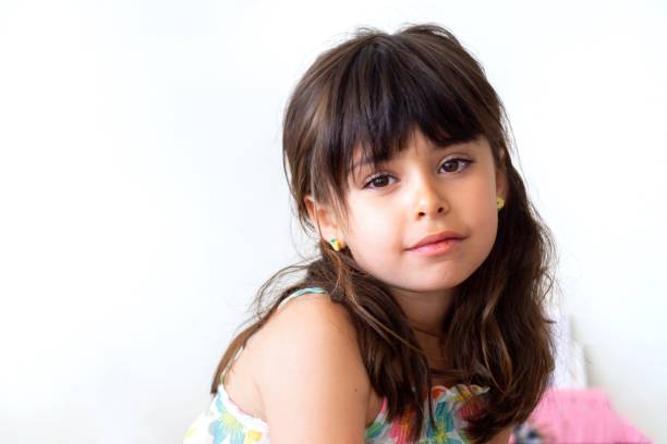 Close view of child with long brown hair, wearing light brown t-shirt, looking at camera with calm expression and slight smile.