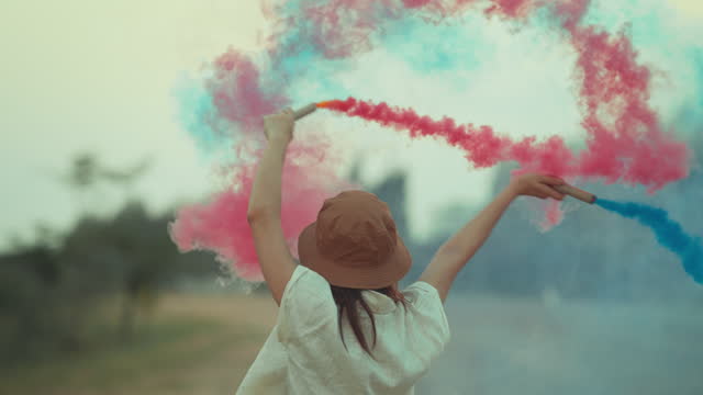 Happy asian woman with blue and pink smoke bombs, female activist portrait with active smoke grenades, freedom with playful dance spin slow motion
