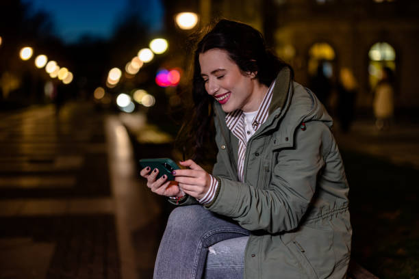 istock Young Woman Captivated by the Game on Her Phone While Sitting on a Bench at Night 1508724031