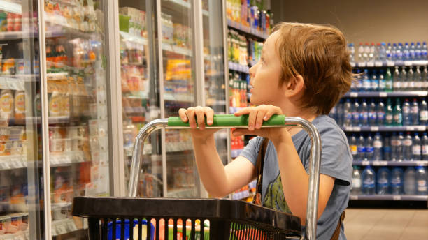Close-up of a cute boy with a shopping trolley looking at the goods in a supermarket stock photo