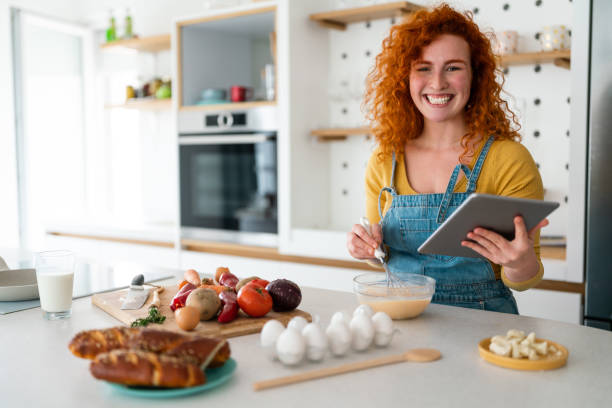 Young woman looking at camera while searching food recipes on digital tablet
