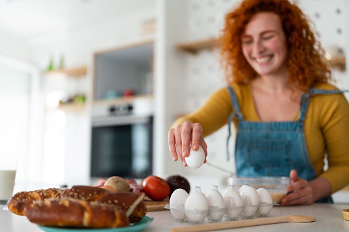 Cheerful young adult woman preparing a healthy meal with eggs in the kitchen and serving bread. Focus is on the food.