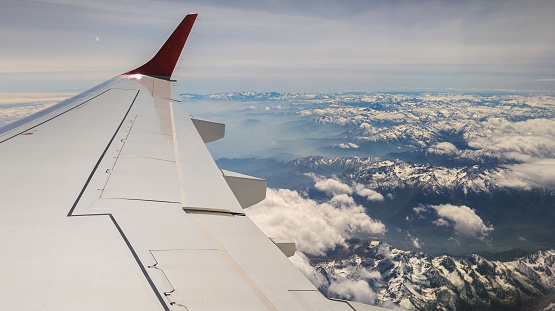 An airplane window view of a mountain range covered with snow and clouds