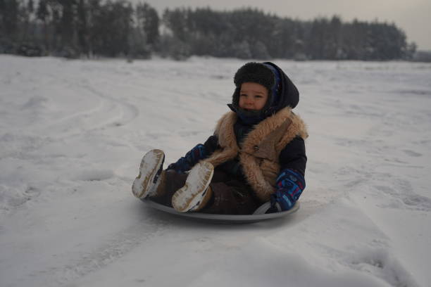 kleine kinder auf schlitten, spaziergänge im winterpark. junge spielt schnee mit den eltern. aufschließen. porträt glückliche kinder - little boys sled clothing slide stock-fotos und bilder