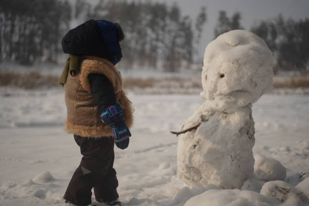 Cute little boy in earflaps hat is making a snowman Cute little boy in earflaps hat is making a snowman ruddy turnstone stock pictures, royalty-free photos & images