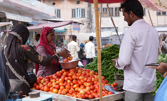 Beawar, Rajasthan, India, July 1, 2023: Rajasthani women purchases tomato from a vendor at a market in Beawar. Vegetable prices have soared across India. Retail price of tomato at Rs 100-120/kg, Garlic at Rs 180-200/kg and Ginger at Rs 240-300/kg in many parts of the country.