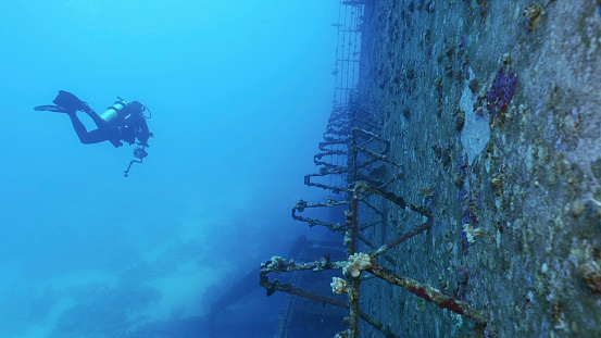 Scuba diver swim along deck of ferry Salem Express shipwreck approaching the ship's superstructure, Red sea, Safaga, Egypt