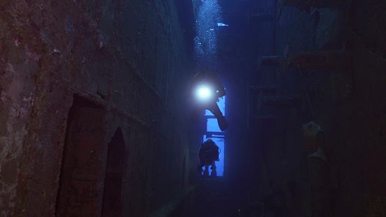 Scuba diver with lantern floats inside of ferry Salem Express shipwreck, Red sea, Safaga, Egypt