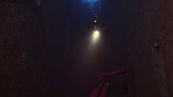 Scuba diver with lantern floats inside of ferry Salem Express shipwreck, Red sea, Safaga, Egypt