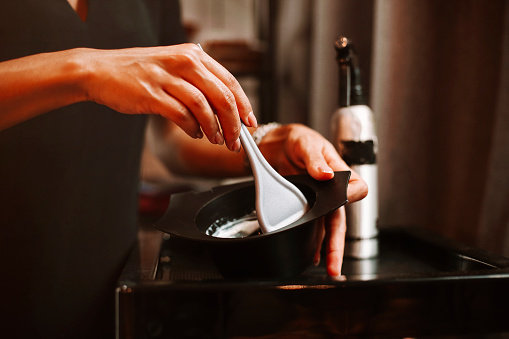 Young hairdresser mixing hair dye in bowl while standing near mirror and woman in modern beauty salon