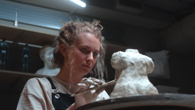 A talented sculptor girl creates a sculpture of a fat woman from clay with her hands. The female strikes with her fingers clay on an figure.