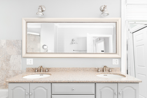 A bathroom detail with a grey vanity cabinet, brown quartz countertop, and lights mounted above the framed mirror.