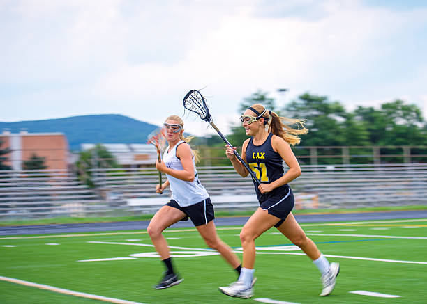 Girls Lacrosse Players Sprint Down Field Towards Ball Panning blur featured as two female La Crosse players from opposing teams race down the field. High degree of motion conveyed. Some motion blur on athletes, particular in extremeties, focus on face of closest player. offense sporting position photos stock pictures, royalty-free photos & images