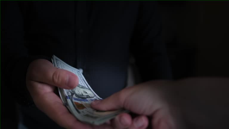 Two men are exchanging money, the man's hand abruptly gives a large wad of cash dollars to the other person